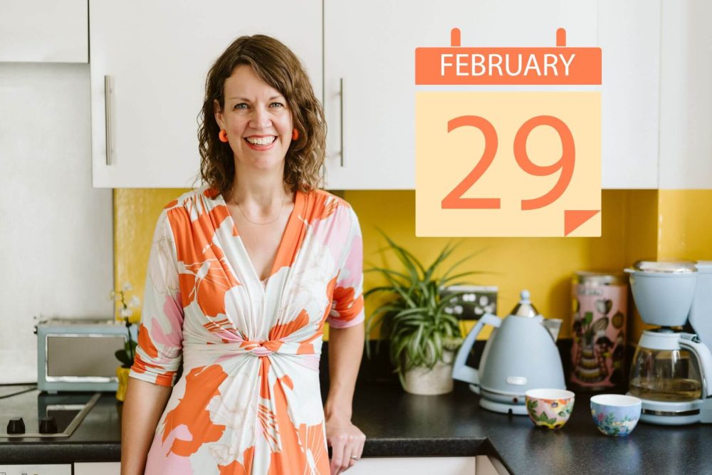 Hester, professional organiser at Tidylicious, in her kitchen with a sign stating "29 February"